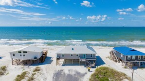 Three beach houses with elevated platforms, a sandy beach, and the ocean in the background. - Gulf Front Retreat | Screened Porch | Fort Morgan Escape (Gulf Shores)