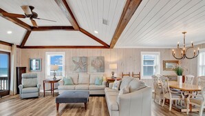 A spacious living room with a high ceiling, wooden beams, a large dining table with chairs, and a view of the ocean through large windows. - Gulf Front Retreat | Screened Porch | Fort Morgan Escape (Gulf Shores)