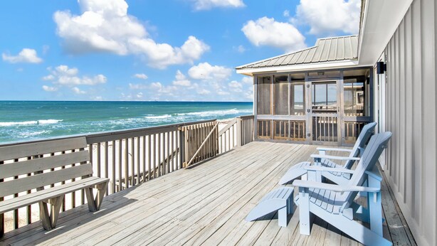 A wooden deck with a view of the ocean, a covered area with Adirondack chairs, and a building with a metal roof. - Gulf Front Retreat | Screened Porch | Fort Morgan Escape (Gulf Shores)