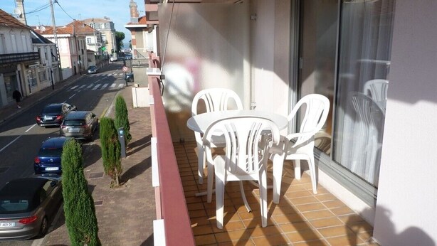 A balcony with white plastic chairs and a table, overlooking a street with parked cars and buildings. - Centre d'Arcachon, emplacement idéal près de la plage (ARCACHON)