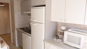 A compact kitchen with a built-in refrigerator, a microwave, a sink, and a small countertop. - Centre d'Arcachon, emplacement idéal près de la plage (ARCACHON)