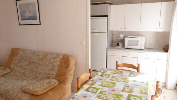 Un petit salon avec un canapé et une table, une cuisine avec des meubles blancs et un four à micro-ondes, et un tableau encadré au mur.