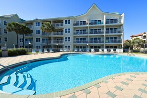 A hotel with a swimming pool, multiple balconies, and a clear blue sky.