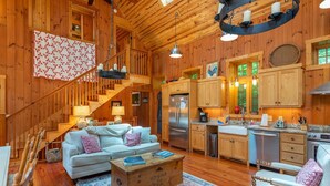 Interior acogedor de una cabaña con escalera de madera, comedor, cocina con electrodomésticos modernos y sala de estar con sofá y mesa de centro.