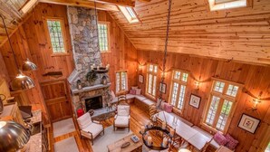Interior acogedor de una cabaña con chimenea de piedra, paredes de madera y comedor con lámpara colgante.