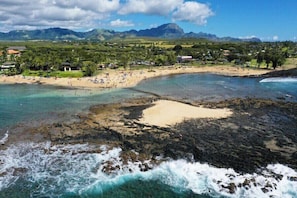 Une plage côtière aux eaux cristallines, avec des zones rocheuses et une chaîne de montagnes en arrière-plan.