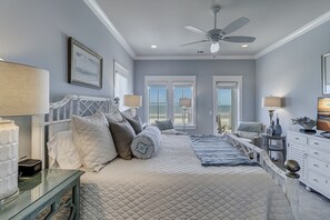 A bedroom with a large bed, two bedside tables, a ceiling fan, and a view of the ocean through the windows. - 31A Dune Lane - This DIRECT oceanfront home will take your breath away! (Hilton Head Island)