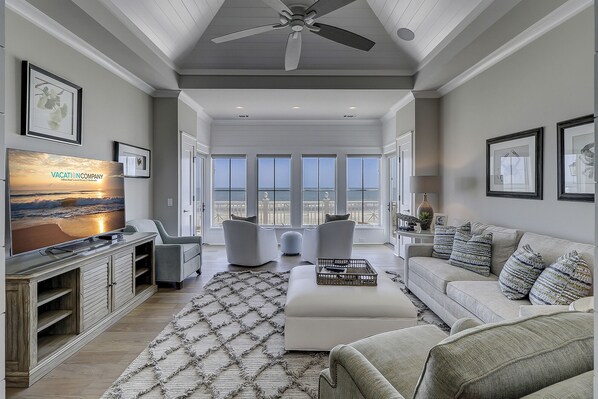 A spacious living room with a large TV, comfortable seating, a ceiling fan, and a view of the ocean. - 31A Dune Lane - This DIRECT oceanfront home will take your breath away! (Hilton Head Island)