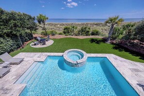 A swimming pool with a hot tub, surrounded by a well-maintained lawn and a view of the ocean.