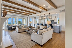 A spacious living room with a high ceiling, wooden beams, and a view of the ocean.