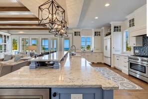 A spacious kitchen with a large island, white cabinetry, and a view to the outdoors.