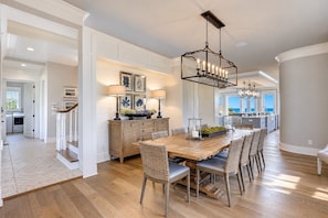 A spacious dining area with a large wooden table and wicker chairs, a kitchen in the background, and a view of the ocean. - 31A Dune Lane - This DIRECT oceanfront home will take your breath away! (Hilton Head Island)