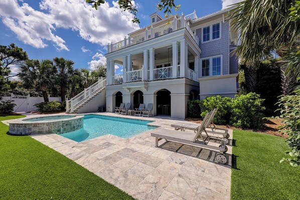 A large, two-story house with a swimming pool, a covered patio, and a well-maintained lawn.