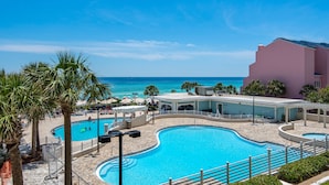 Zwembad van een resort met helder uitzicht op de oceaan, omringd door palmbomen en een gebouw met een roze gevel.
