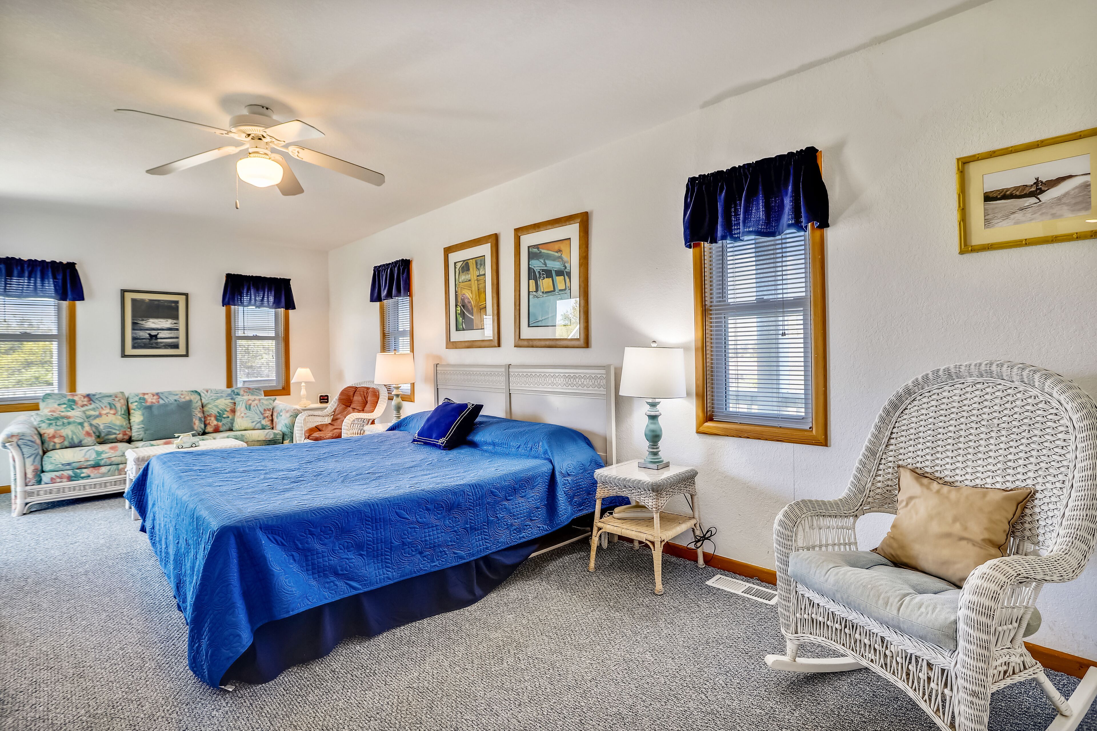 A bedroom with a bed, a rocking chair, a chair, a sofa, and a ceiling fan.