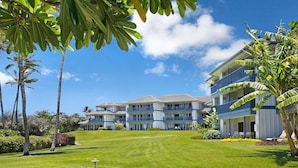 A hotel with multiple floors, a well-maintained lawn, and palm trees. - Poipu Sands 123 Beautiful Ocean View AC Suite Paradise (Koloa)