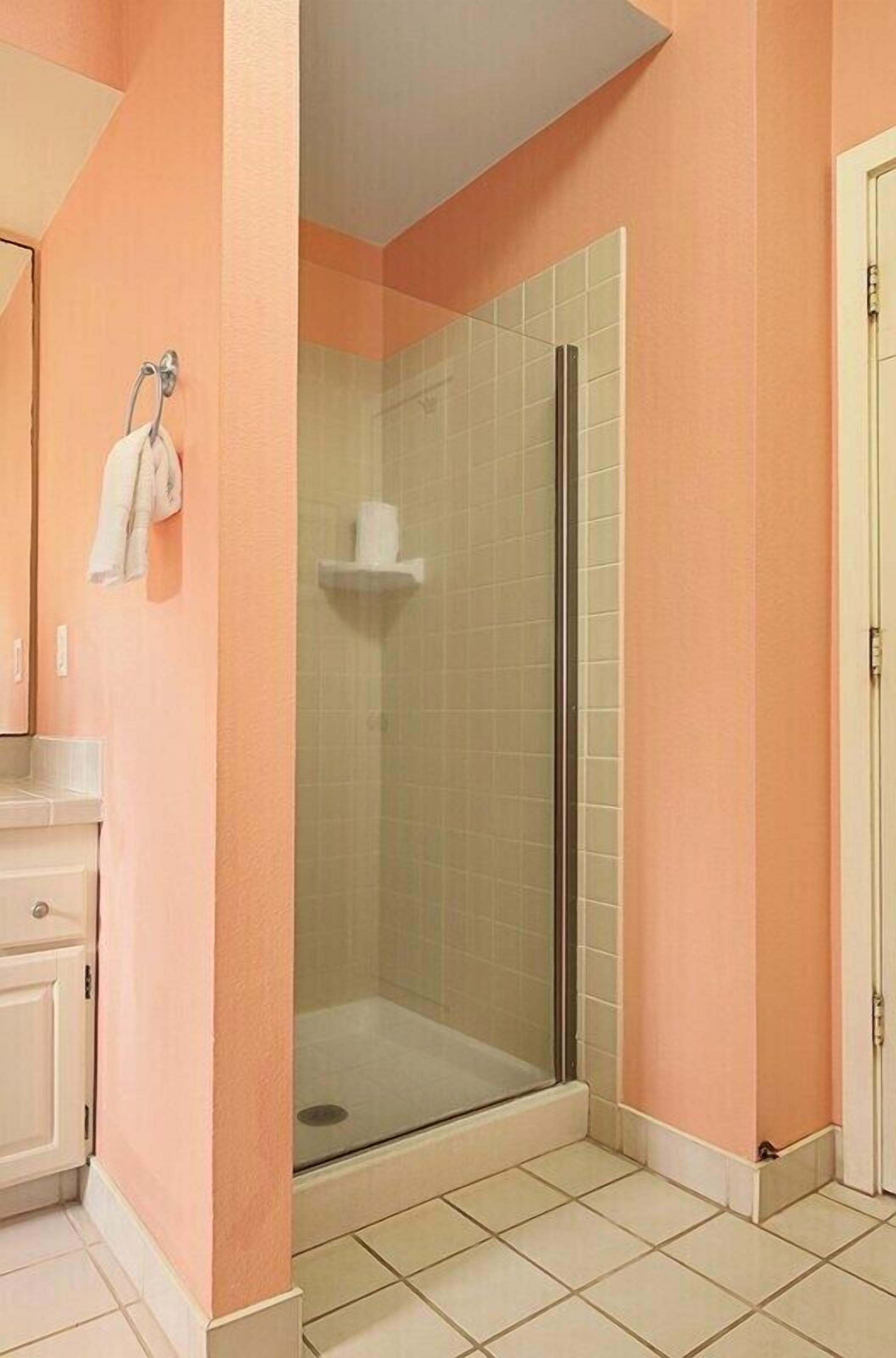 Een badkamer met een douchecabine van glas, een witte wastafel en een handdoekrek.