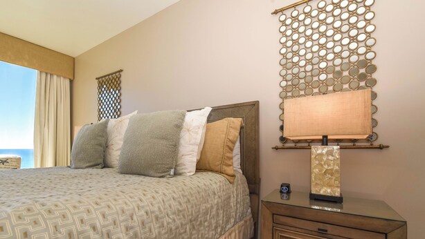 A neatly made bed with patterned bedding, a bedside table with a lamp, and a decorative wall piece. - Modern Coastal Beachfront Condo w/ Expansive Balcony at Silver Beach Towers! 🏖️ (Destin)