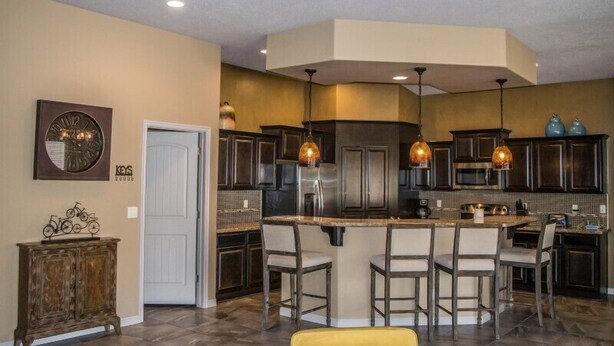 A modern kitchen with dark cabinetry, a central island with bar stools, pendant lighting, and a decorative clock on the wall.