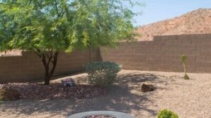 A stone fire pit in a landscaped outdoor area with a tree and a brick wall in the background.