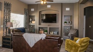 A living room with a brown leather sofa, a yellow armchair, a ceiling fan, a flat-screen TV, and a fireplace.