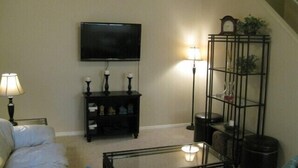 A living room with a flat-screen TV, a black entertainment unit with candles, a glass coffee table, and a sofa with cushions.