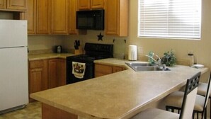A kitchen with wooden cabinets, a black stove, a microwave, a refrigerator, a sink, and a window with blinds.