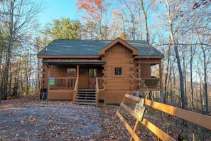 A cabin with a porch, a small staircase, and a wooden fence in front.