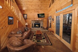 A cozy cabin interior with a wooden interior, a fireplace, leather furniture, and a large window.