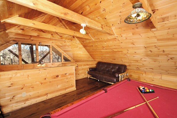 A wooden interior with a pool table, leather sofa, and a ceiling fan.