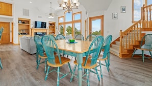 A spacious living room with a wooden dining table, teal chairs, and a chandelier. - As Time Goes By: Dog-friendly, Elevator, Pool, Hot Tub (Corolla)
