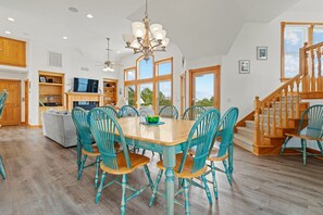 A spacious living room with a wooden dining table, teal chairs, and a chandelier. - As Time Goes By: Dog-friendly, Elevator, Pool, Hot Tub (Corolla)