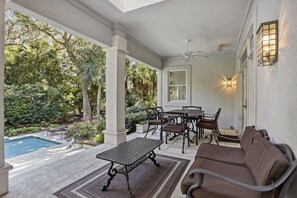 Un patio couvert avec une piscine, du mobilier d’extérieur et une vue sur un jardin luxuriant.