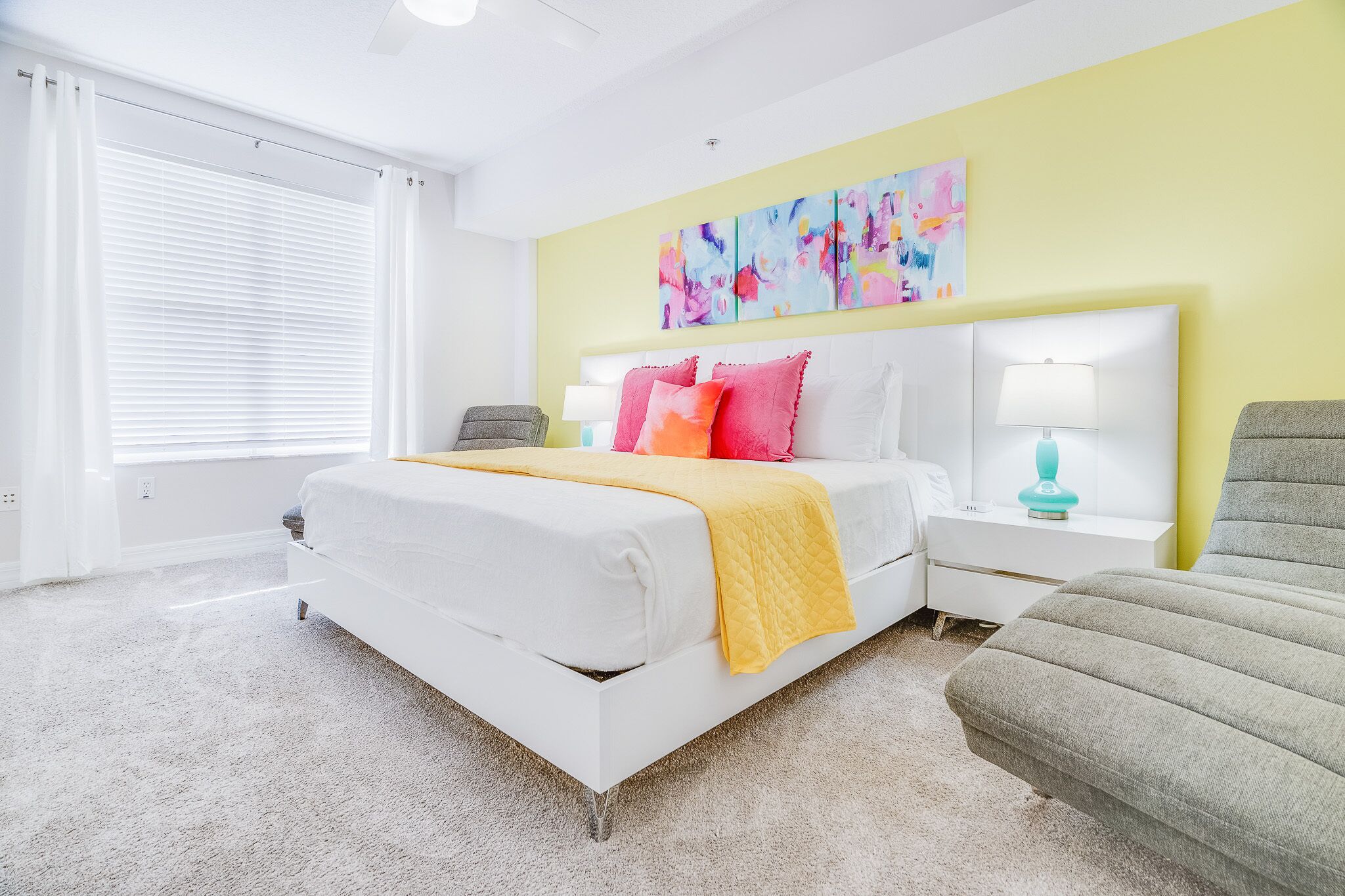 A modern bedroom with a large bed, a bedside table with a lamp, and a colorful abstract painting on the wall.