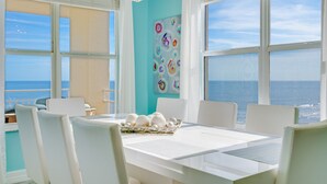 A dining area with a view of the sea, a white table, and chairs.