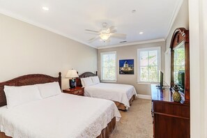 Quarto com duas camas, um ventilador de teto e uma escrivaninha com abajur.