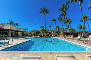 A swimming pool with clear blue water, surrounded by palm trees and lounge chairs.