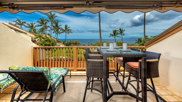 Un patio techado con mesa y sillas, con vista a palmeras y al océano.