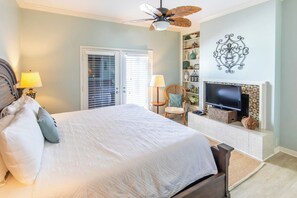 A bedroom with a bed, a television, a fireplace, and a ceiling fan.