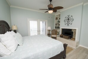 Quarto com cama, ventilador de teto, lareira e televisão.