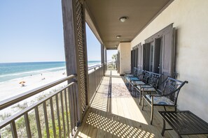 Um deck de madeira com vista para a praia e oceano. Há cadeiras de metal e um banco ao longo do corrimão.