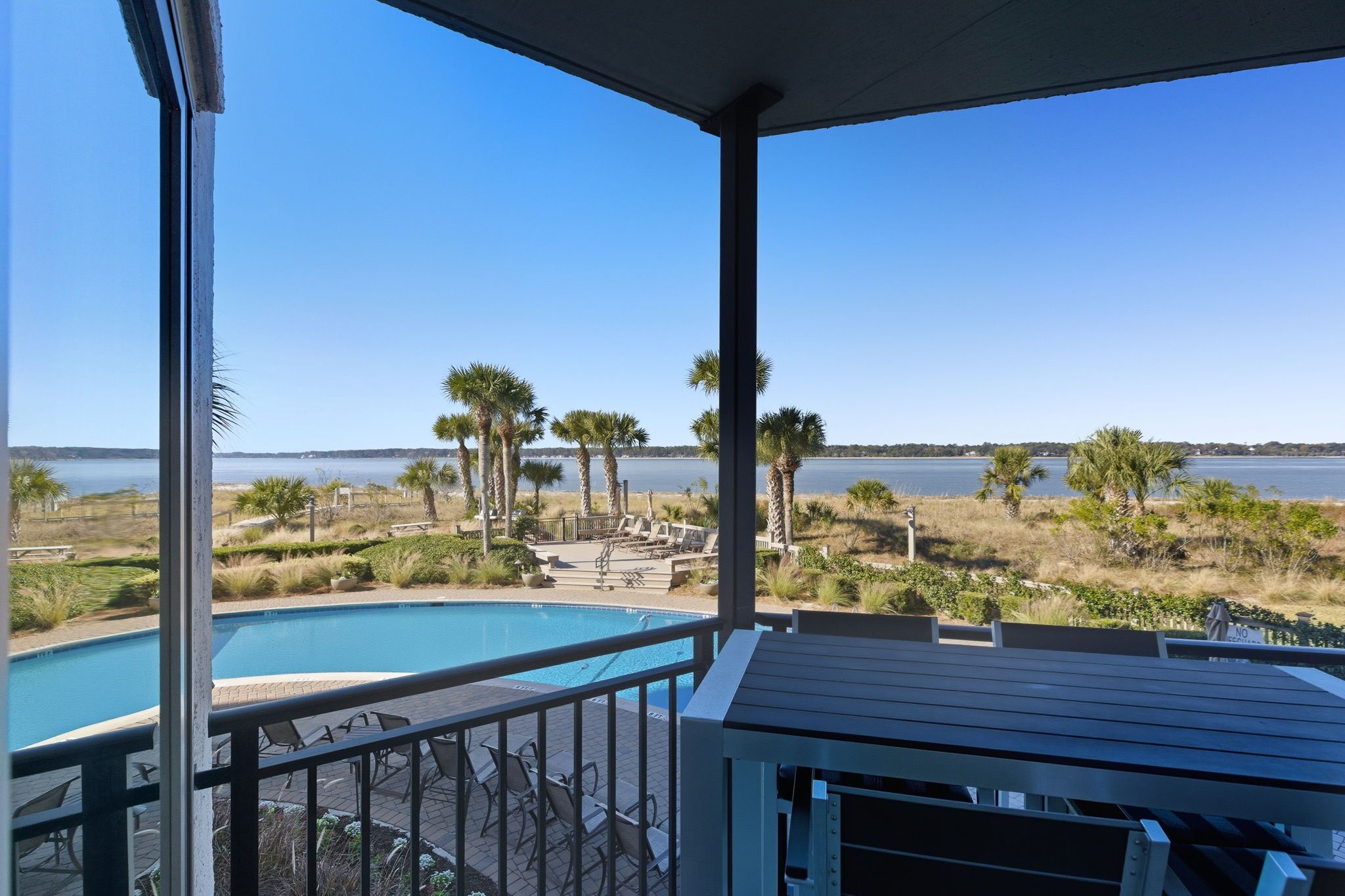 Une vue sur la piscine, avec une vue dégagée sur l’eau, les palmiers et une côte lointaine.