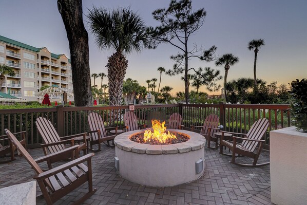 An outdoor seating area with a fire pit surrounded by wooden chairs and a stone fire table. - Gorgeous  two bedroom end unit villa in Palmetto Dunes on Hilton Head Island (Hilton Head Island)