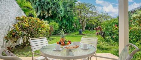A patio with a round table and four chairs, surrounded by lush greenery and a white wall.