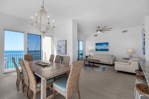 A spacious living area with a dining table, wicker chairs, a sofa, and a ceiling fan.