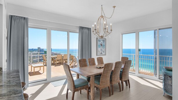A spacious dining area with a large table and chairs, large windows with a view of the ocean, and a chandelier.