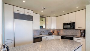 A modern kitchen with white cabinets, granite countertops, a built-in microwave, and a dishwasher. - Beachfront Living - Makena Surf E-202 - Mesmerizing Views & Tropical Landscapes (Makena, Maui)