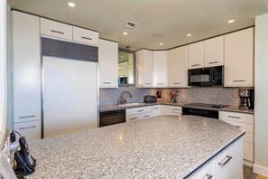 A modern kitchen with white cabinets, granite countertops, a built-in microwave, and a dishwasher. - Beachfront Living - Makena Surf E-202 - Mesmerizing Views & Tropical Landscapes (Makena, Maui)