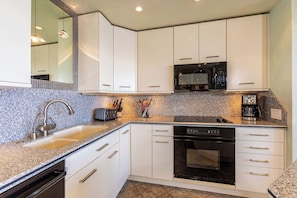 A modern kitchen with white cabinets, a granite countertop, a built-in oven, a microwave, and a coffee maker.