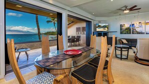 A modern dining area with a glass table, wooden chairs, and a view of the ocean. - Beachfront Living - Makena Surf E-202 - Mesmerizing Views & Tropical Landscapes (Makena, Maui)